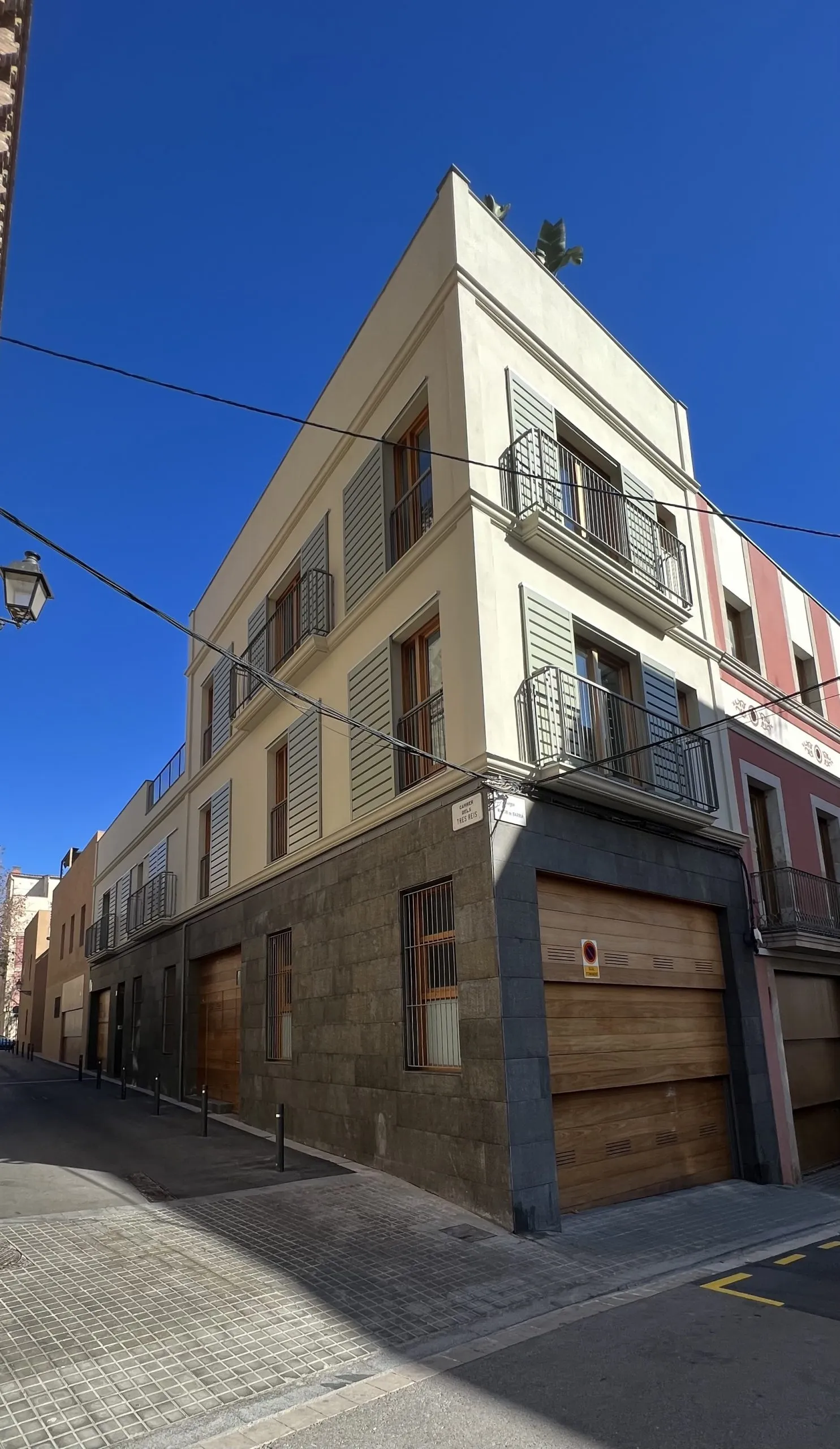 Casa en esquina terminada en Sarrià, con fachada de estuco claro, zócalo de piedra y persianas verde salvia